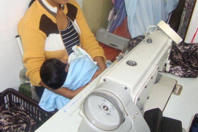 Jovem cuida do filho recém nascido enquanto trabalha. O carrinho fica ao lado da máquina de costura na Zona Norte da capital paulista (SRTE-SP)