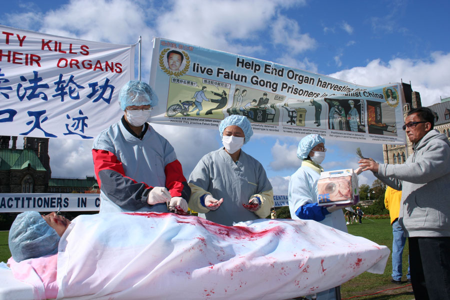 Uma cena da extração forçada de órgãos de praticantes do Falun Gong na China é representada durante uma manifestação em Ottawa, Canadá, em 2008. Evidências recentes indicam a criação de uma nova base de dados de DNA para compatibilidade de transplante de órgãos, constituída de amostras de DNA recolhidas de praticantes do Falun Gong fora do sistema de detenção ou prisões na China (Epoch Times)