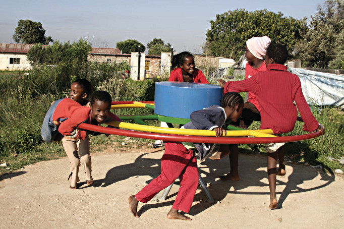 Crianças brincando num gira-gira e, aos mesmo tempo, bombeando água.