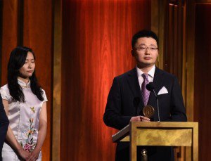 Diretor Leon Lee recebendo o prêmio no palco com Crystal Chen, uma praticante de Falun Gong, a seu lado (Ilya S. Savenok Getty Images para Peabody Awards)