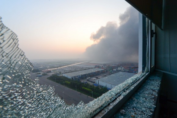   Fogo e fumaça são vistos de uma janela quebrada em um apartamento perto do local das explosões massivas em Tianjin, China, em 13 de agosto (STR / AFP / Getty Images)