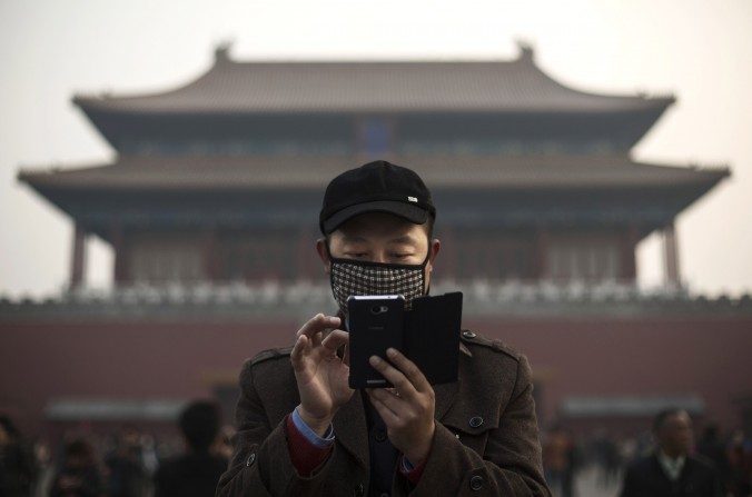 Um chinês usa seu celular num dia nebuloso em frente da Cidade Proibida, em Pequim, em 20 de novembro de 2014 (Kevin Frayer/Getty Images)