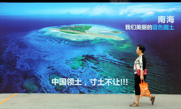 Foto tirada em 14 de julho de 2016 mostra mulher passando próxima de um cartaz mostrando o Mar da China Meridional, com o slogan na parte inferior: "Território da China, nunca vamos ceder uma polegada de nossa terra" em uma rua de Weifang, na província oriental de Shandong, na China. (STR/AFP/Getty Images)