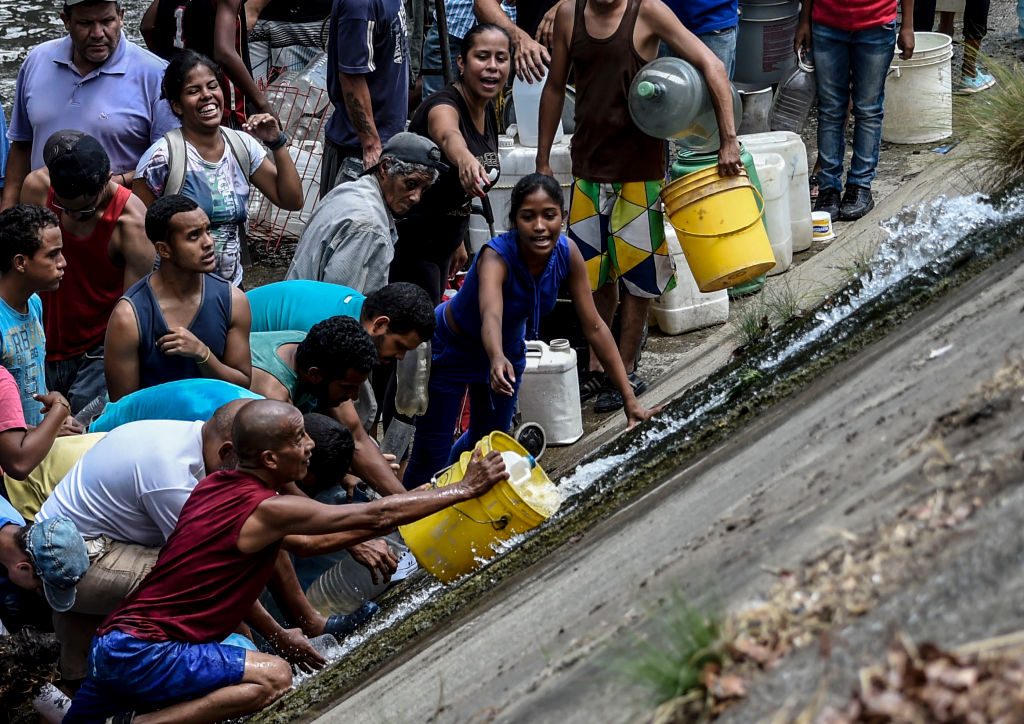 Pessoas coletam água de um canal de esgoto no rio Guaire, em Caracas, em 11 de março de 2019, enquanto um blecaute em massa continua afetando algumas áreas do país (JUAN BARRETO / AFP / Getty Images)