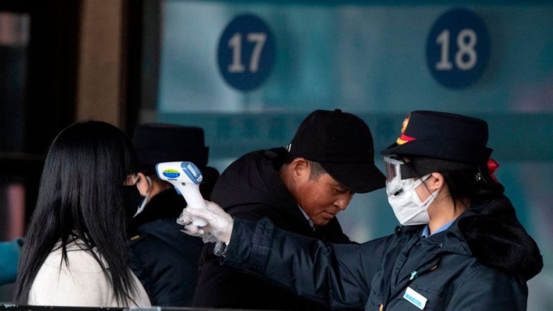 Foto tirada em 1 de fevereiro de 2020, revela  o pessoal de segurança verificando a temperatura de um passageiro com uma máscara na estação ferroviária de Pequim.  O número de infecções no surto de coronavírus na China aumentou de 14.300 em todo o país, com 2.590 novos casos confirmados, informou a Comissão Nacional de Saúde em 2 de fevereiro (Foto de NOEL CELIS / AFP) (Foto de NOEL CELIS/AFP vía Getty Images)