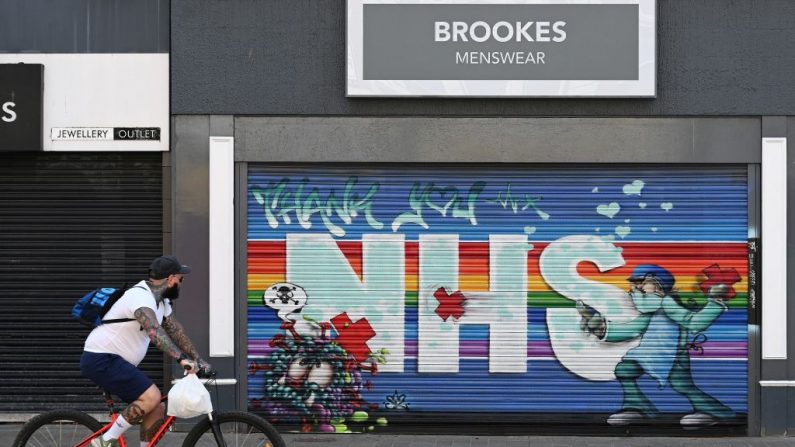 Um ciclista passa um mural de grafite de arte de rua em apoio ao NHS (Serviço Nacional de Saúde) nas persianas de uma loja fechada em Hull, norte da Inglaterra em 9 de maio de 2020, enquanto a vida na Grã-Bretanha continua no fim de semana do feriado bancário de maio, durante o bloqueio em todo o país devido à nova pandemia de coronavírus COVID-19 (Foto por PAUL ELLIS / AFP via Getty Images)
