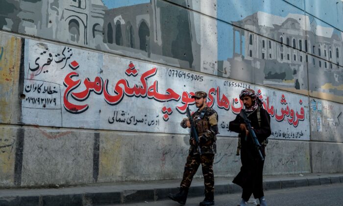 Patrulha Talibã ao longo de uma rodovia tendo como pano de fundo um mural pintado na parede de um viaduto em Cabul em 26 de setembro de 2021 (Hoshang Hashimi / AFP via Getty Images)
