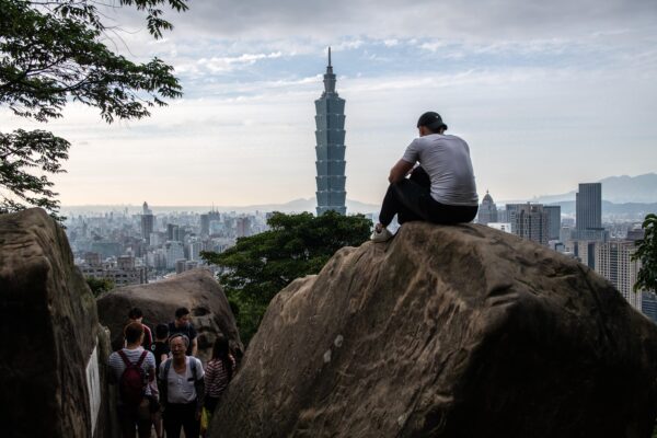 Homem sentado em uma rocha com vista para a torre Taipei 101 e o horizonte de Taipei no topo da Elephant Mountain, em 7 de janeiro de 2020, na cidade de  Taipei, em Taiwan (Carl Court / Getty Images)
