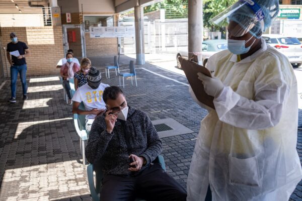 Um profissional de saúde ajuda um paciente a preencher um formulário antes de realizar um teste PCR para a COVID-19, no laboratório Lancet, em Joanesburgo, em 30 de novembro de 2021 (EMMANUEL CROSET / Getty Images)