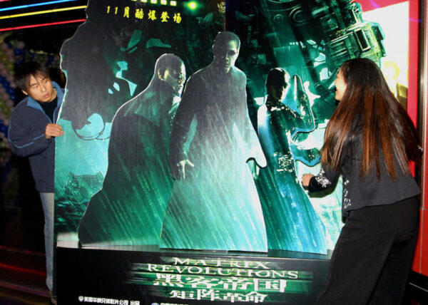 Funcionários do cinema colocam banner do filme "Matrix: Revolutions", em Pequim, no dia 5 de novembro de 2003. Milhões de pessoas aguardam ansiosamente o lançamento de “Matrix: Revolutions”, o terceiro da trilogia de ficção científica estrelada por Keanu Reeves (STR/AFP via Getty Images)