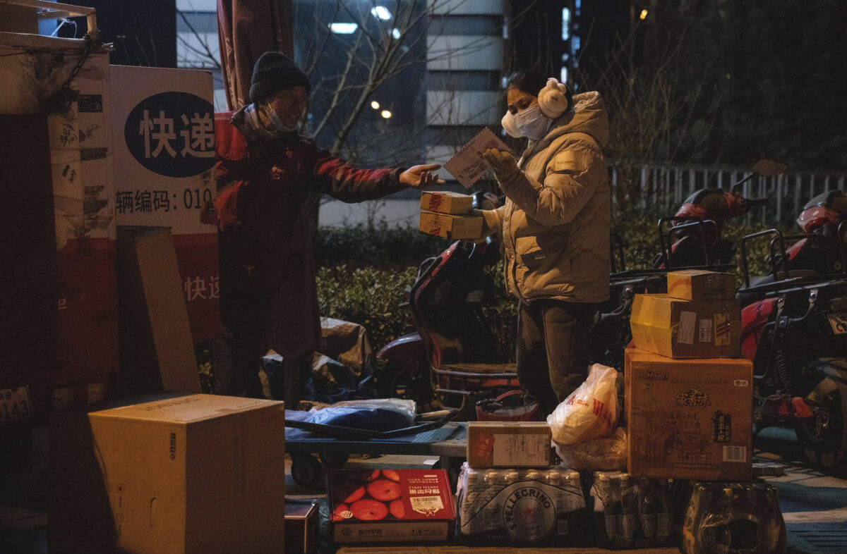  Uma mulher utilizando uma máscara para se proteger do coronavírus olha para um pacote perto de um entregador em Pequim, na China, no dia 18 de janeiro de 2022 (AP Photo/Ng Han Guan)
