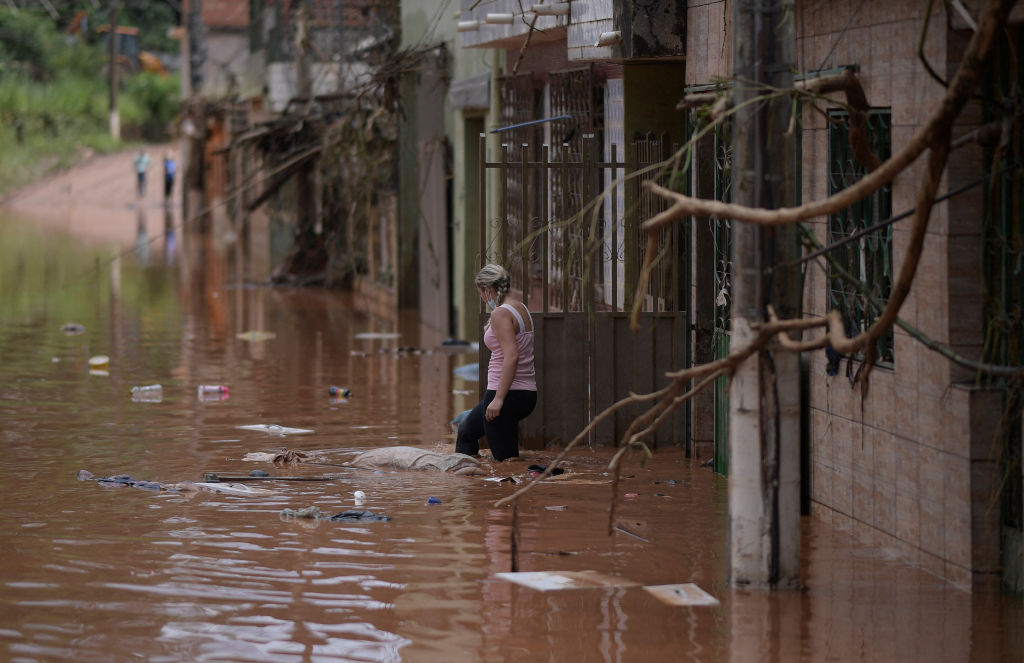 Uma mulher percorre as águas contra a enchente que começa a recuar no município brasileiro de Raposos, localizado no estado de Minas Gerais, no dia 11 de janeiro de 2022, após fortes chuvas que ocorreram nos últimos dias, no sul do país (DOUGLAS MAGNO/AFP via Getty Images)