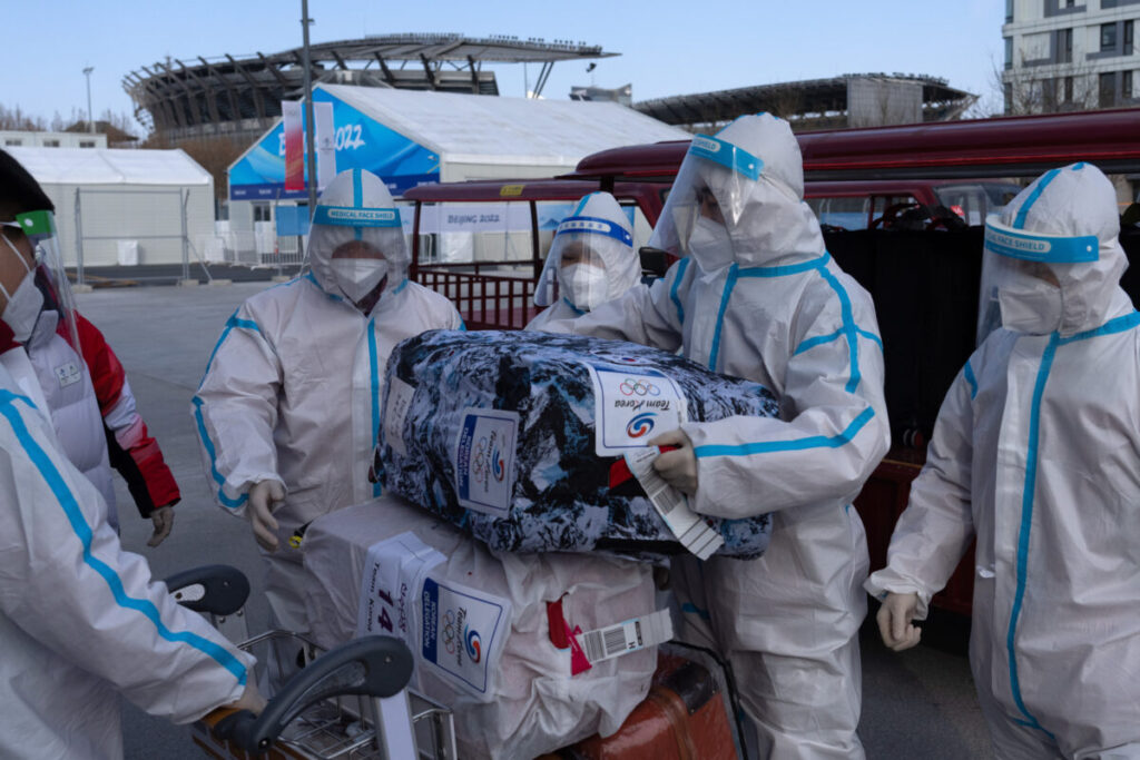 Funcionários utilizando equipamentos de proteção individual carregam bagagens pertencentes a membros da equipe da Coreia do Sul, em carrinhos na Vila Olímpica, antes dos Jogos Olímpicos de Inverno em Pequim de 2022, no dia 31 de janeiro de 2022 (Carl Court/Getty Images)