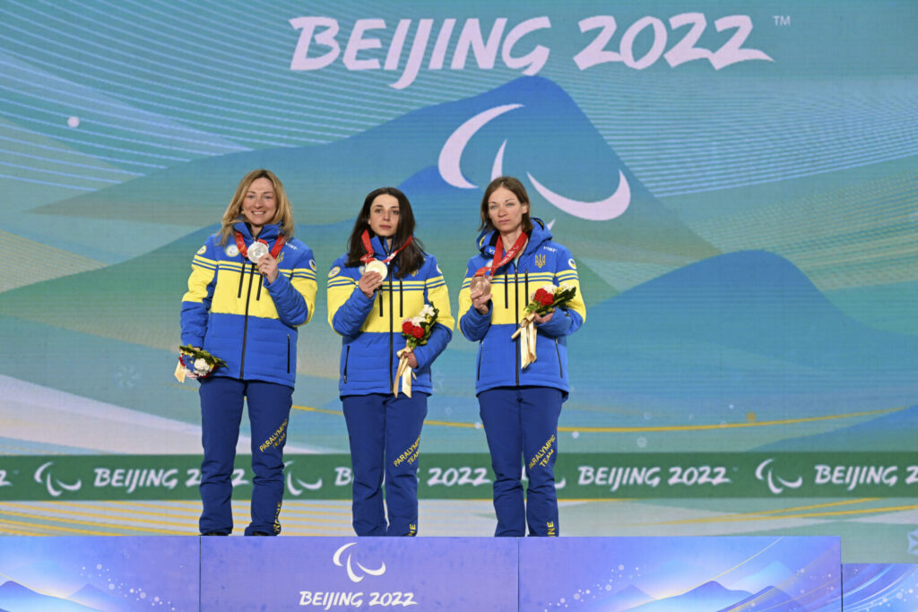 A medalhista de ouro Iryna Bui da Equipe Ucrânia (C), a medalhista de prata Oleksandra Kononova da Equipe Ucrânia (E) e a medalhista de bronze Liudmyla Liashenko da Equipe Ucrânia (D) comemoram durante a cerimônia de medalhas de distância média do biatlo feminino no Zhangjiakou Medals Plaza, no quarto dia das Jogos Paralímpicos de Inverno em Pequim, em Zhangjiakou, na China, no dia 8 de março de 2022 (Zhe Ji/Getty Images)