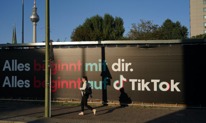 Uma jovem segurando um smartphone passa por um anúncio da empresa de mídia social TikTok em Berlim, Alemanha, em 21 de setembro de 2020 (Sean Gallup/Getty Images)