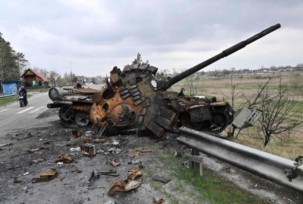 Um homem passa de moto por um tanque russo destruído em uma estrada no vilarejo de Rusaniv, perto de Kiev, na Ucrânia, em 16 de abril de 2022 (Genya Savilov/AFP/Getty Images)