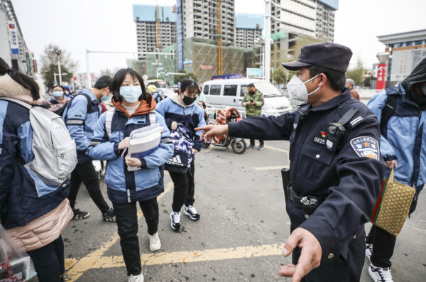 Um policial gesticula na entrada de uma escola enquanto estudantes do ensino fundamental e médio retornam após atrasos devido ao surto de vírus do PCCh em Huaian, província de Jiangsu, em 30 de março de 2020 (STR/AFP via Getty Images