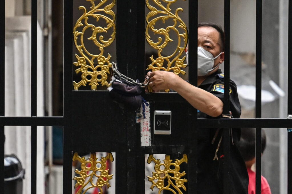 Um funcionário de segurança tranca uma porta com uma corrente em um bairro sob um lockdown da COVID-19 no distrito de Jing'an, em Xangai, em 2 de junho de 2022 (Hector Retamal/AFP via Getty Images)