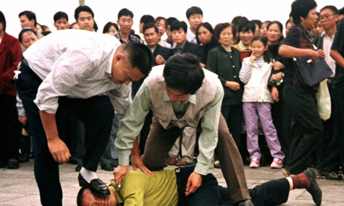 Policiais vestidos com roupas simples lidam com um manifestante do Falun Gong na Praça Tiananmen, em Pequim, enquanto uma multidão assiste, em 1º de outubro de 2000 (Chien-min Chung/AP)