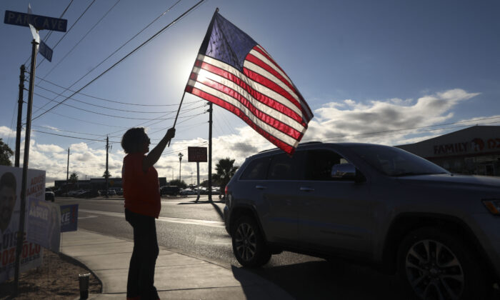 Uma mulher agita uma bandeira americana para cumprimentar os motoristas enquanto se dirigem para votar nas eleições de meio de mandato dos EUA no Centro Cultural Cesar Chavez em San Luis, Arizona, em 8 de novembro de 2022. (Sandy Huffaker/AFP via Getty Images)