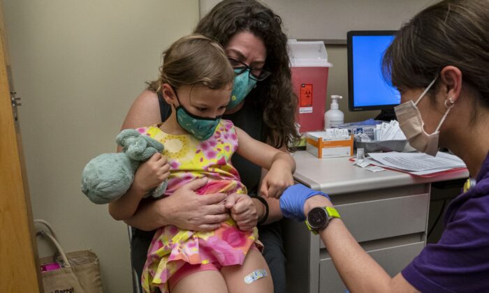 Nora Burlingame, 3 anos, senta-se no colo de sua mãe, Dina Burlingame, é cumprimentada pela enfermeira Luann Majeed, após receber sua primeira dose da vacina Pfizer COVID-19 no UW Medical Center-Roosevelt em Seattle, Washington, em 21 de junho de 2022 (David Ryder/Getty Images)