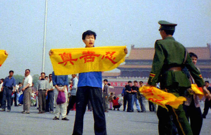 Um policial chinês se aproxima de um praticante do Falun Gong na Praça da Paz Celestial em Pequim enquanto ele segura uma faixa com os caracteres chineses de "verdade, compaixão e tolerância", os princípios fundamentais do Falun Gong. (Cortesia de Minghui.org)