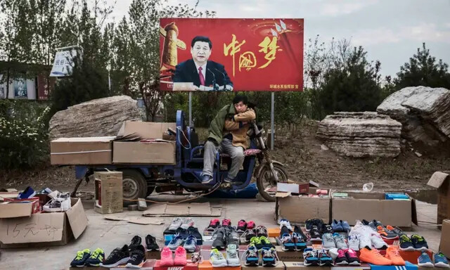 Um vendedor chinês vende tênis e sapatos na rua em frente a uma placa mostrando o líder chinês Xi Jinping com "China Dream" escrito nele, em Shijiazhuang, província de Hebei, China, em 9 de abril de 2017. (Kevin Frayer/ Getty Images)