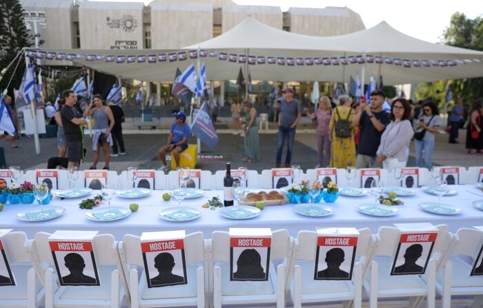 Pessoas ao lado de uma instalação artística de uma longa mesa de jantar Shabat com a palavra Refém em todas as cadeiras em homenagem aos israelenses sequestrados por militantes do Hamas durante os ataques de 7 de outubro, em Tel Aviv, Israel, 21 de outubro de 2023 (EFE/EPA/ABIR SULTAN )