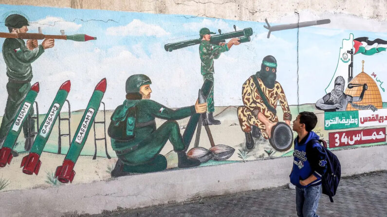 Uma criança passa por um mural que retrata soldados disparando foguetes enquanto os palestinos marcam o 34º aniversário da fundação do movimento islâmico Hamas que governa a faixa palestina, em 11 de dezembro de 2021 (Disse Khatib/AFP via Getty Images)
