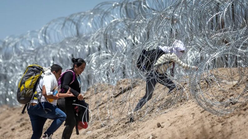 Imigrantes ilegais passam por arame farpado em torno de um campo improvisado de migrantes após cruzarem a fronteira do México, em El Paso, Texas, em 11 de maio de 2023. (John Moore/Getty Images)
