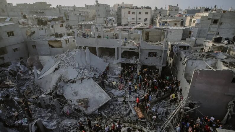 Civis palestinos e equipes de resgate vasculham os escombros de um prédio desabado em Al-Maghazi, localizado no centro da Faixa de Gaza, em busca de sobreviventes e vítimas após o bombardeio israelense em 5 de novembro de 2023. (Mohammed Zaanoun/Middle East Images/ AFP via Getty Images)
