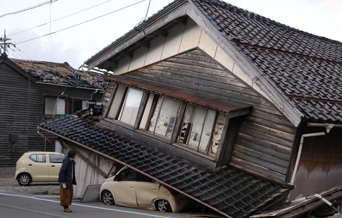 Uma mulher olha para uma casa e veículos danificados após um forte terremoto na cidade de Tohi, Península de Noto, Japão, em 2 de janeiro de 2024. (EFE/FRANCK ROBICHON)