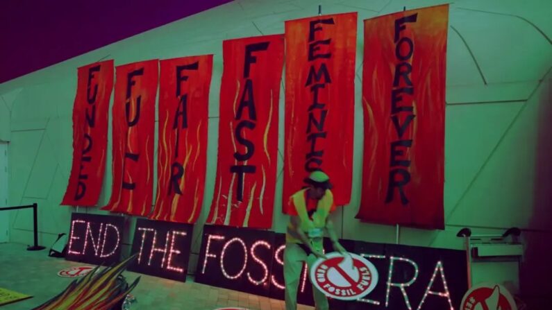 Um ativista coloca cartazes de protesto no chão ao lado de um cartaz iluminado que diz: "End the fossil era" (Acabar com a era fóssil) após um protesto para exigir a eliminação gradual dos combustíveis fósseis no décimo segundo dia da Conferência do Clima COP28 da UNFCCC em Dubai, Emirados Árabes Unidos, em 12 de dezembro de 2023. (Sean Gallup/Getty Images)