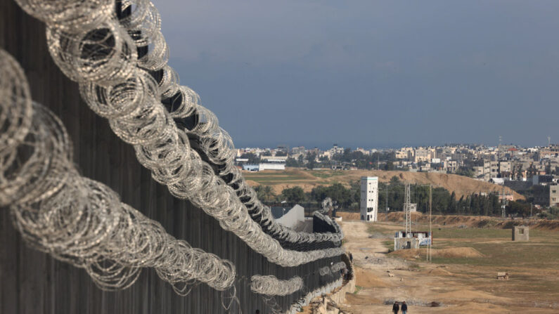 Palestinos deslocados caminham ao lado da cerca da fronteira entre Gaza e Egito, em 16 de fevereiro de 2024, em Rafah, no sul da Faixa de Gaza, em meio ao conflito em curso entre Israel e o grupo militante palestino Hamas (Foto de MOHAMMED ABED/AFP via Getty Images)