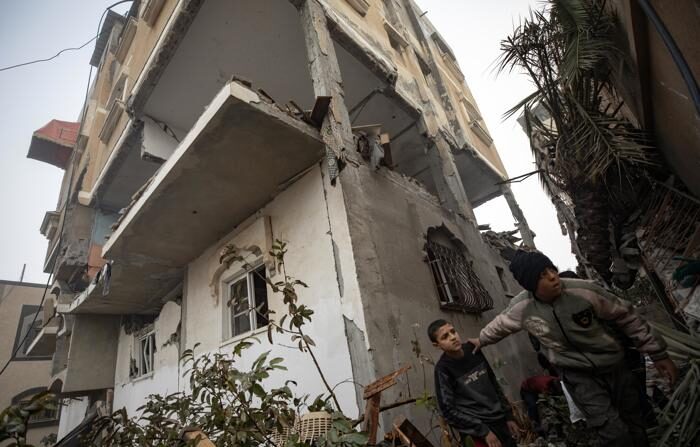 Crianças palestinas passam por um prédio danificado após um ataque aéreo israelense no campo de refugiados de Rafah, no sul da Faixa de Gaza, em 9 de fevereiro de 2024 (EFE/EPA/Haitham Imad)