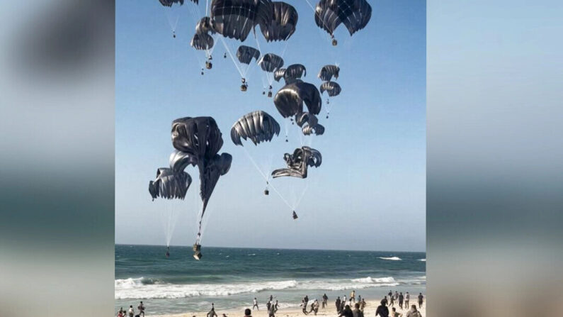 Palestinos correm em direção a pára-quedas presos a pacotes de alimentos, lançados de aeronaves dos EUA em uma praia na Faixa de Gaza em 2 de março de 2024 (AFP via Getty Images)

