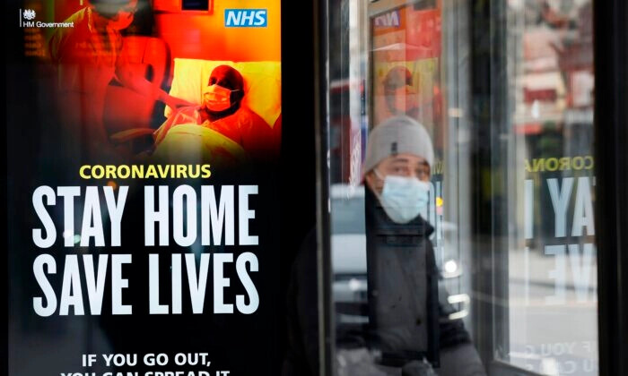 Um passageiro usa uma máscara enquanto está sentado em um abrigo de ônibus com o sinal do NHS promovendo "Stay Home, Save Lives" em Chinatown, centro de Londres, em 8 de janeiro de 2021. (Tolga Akmen /AFP via Getty Images)
