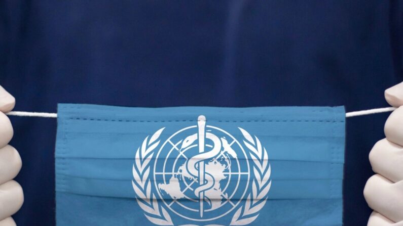 Um médico segura uma máscara facial médica com a bandeira da Organização Mundial da Saúde. (kcube-Baytur/Shutterstock)