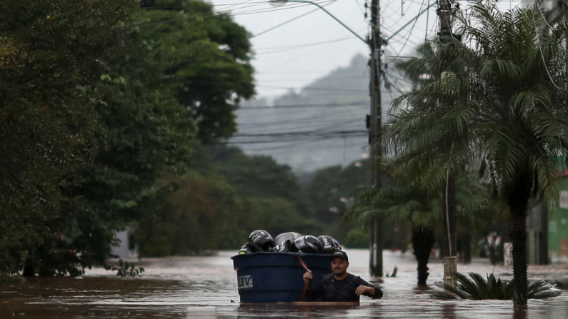 Um homem usa um tanque de água para carregar seus pertences em uma rua inundada no centro da cidade de São Sebastião do Cai, no estado do Rio Grande do Sul, Brasil, em 2 de maio de 2024 (Foto de ANSELMO CUNHA/AFP via Getty Images)