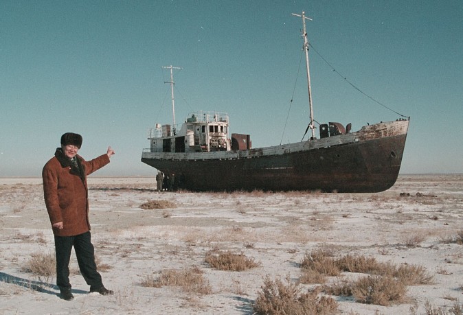 Aralsk's Mayor Alashbai Baimyrzayev points 23 March 1999 near the city of Kyzmet, a fishery on Aralsk's dry harbor at an abandoned fishermen ship in Aral Sea. Aral Sea, an inland sea, East of the Caspian Sea, mainly in Kazakhstan is world's fourth largest lake. Originally 65,000 sq km/25,000 sq mi, 420 km/260 mi long, 280 km/175 mi wide, maximum depth 70 m/230 ft, Aral Sea contains several small island. The diversion of water from rivers supplying the sea for cotton irrigation projects has seriously upset ecological balance and the sea shrank by nearly three-fourths an dropped 19 meters over three decades. / AFP / STRINGER (Photo credit should read STRINGER/AFP/Getty Images)