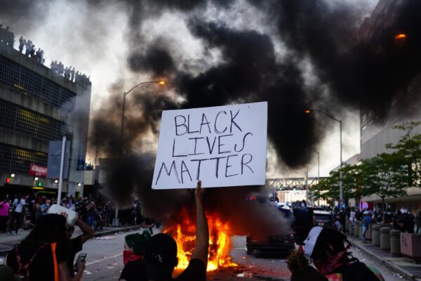 Um homem segura um pôster Black Lives Matter enquanto um carro da polícia queima durante um protesto em frente ao CNN Center em 29 de maio de 2020, em Atlanta, Geórgia (Elijah Nouvelage / Getty Images)