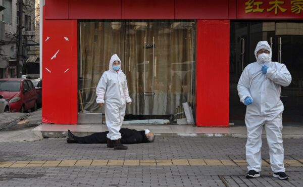 Autoridades chinesas em trajes de proteção revistam um idoso com máscara facial que desmaiou e morreu em uma rua perto de um hospital em Wuhan, China, em 30 de janeiro de 2020 (HECTOR RETAMAL / AFP via Getty Images)