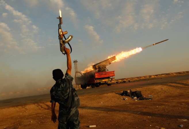 Um guerrilheiro rebelde comemora enquanto seus camaradas ateiam fogo a uma bateria de mísseis contra as posições das tropas leais ao líder líbio Muammar Kadafi em 14 de abril de 2011, a oeste de Ajdabiyah, Líbia. Os rebeldes trocaram tiros e mísseis com tropas leais a oeste de Ajdabiyah em 14 de abril de 2011, enquanto o conflito que envolvia a Líbia continuava (Chris Hondros/Getty Images)
