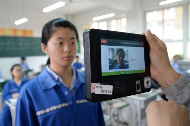 Um professor usa uma máquina que emprega tecnologia de reconhecimento facial e impressão digital para verificar a identificação de um aluno antes de um exame simulado de admissão na faculdade da cidade de Handan, província de Hebei, China, em 6 de junho de 2017. (STR/AFP/Getty Images)