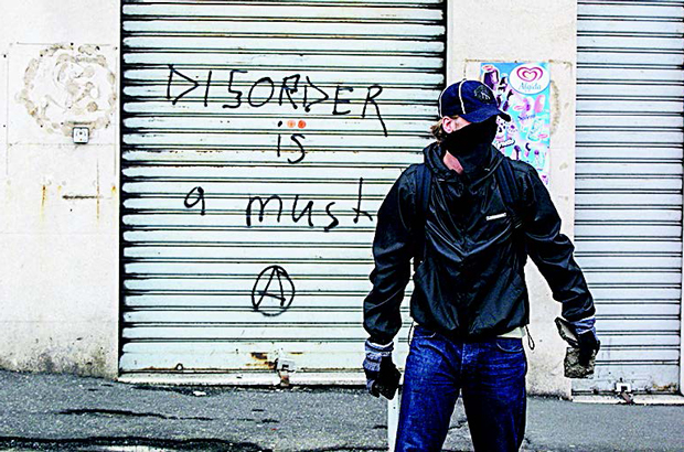 Um manifestante de extrema esquerda maneja pedras em frente de um grafite que diz "Desordem é uma necessidade" com um símbolo anarquista embaixo, durante uma reunião do G-8 em Gênova, Itália, em 2001 (Sean Gallup/Getty Images)